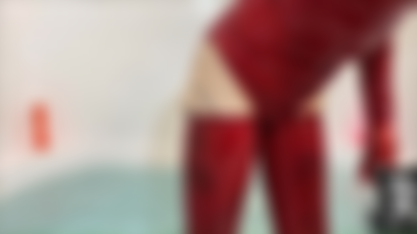 Che cavalca un palloncino rosso nella vasca e indossa un body e calze in lattice rosso.
