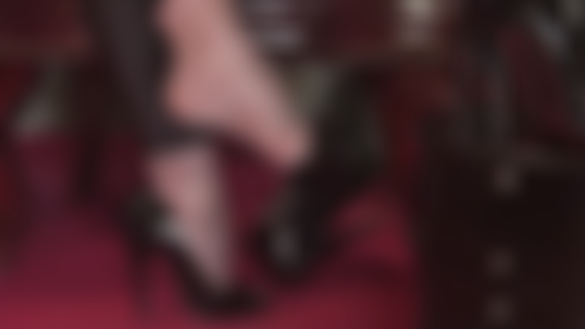 Primo piano dei piedi della padrona che penzolano da scarpe lucide con punta aperta e collant grigi super lucidi.