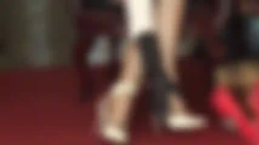 Sandali bianchi con cinturini e collant lucidi che stuzzicano i piedi.