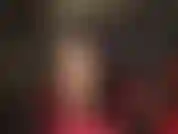 Sexy, con collant color carne che stuzzicano le gambe, capelli neri, pelle nera, body rosso e tacchi a spillo rossi con cinturino alla caviglia.