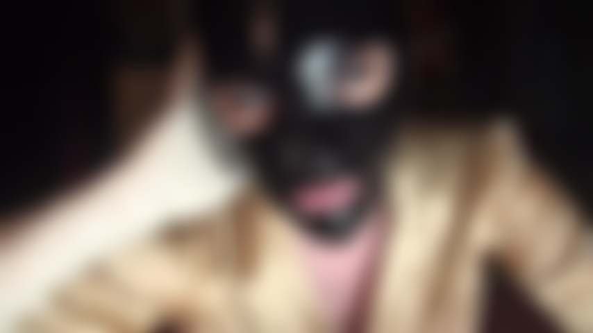 Feticista del lattice: cappuccio di gomma nera lucida e guanti di lattice bianchi.