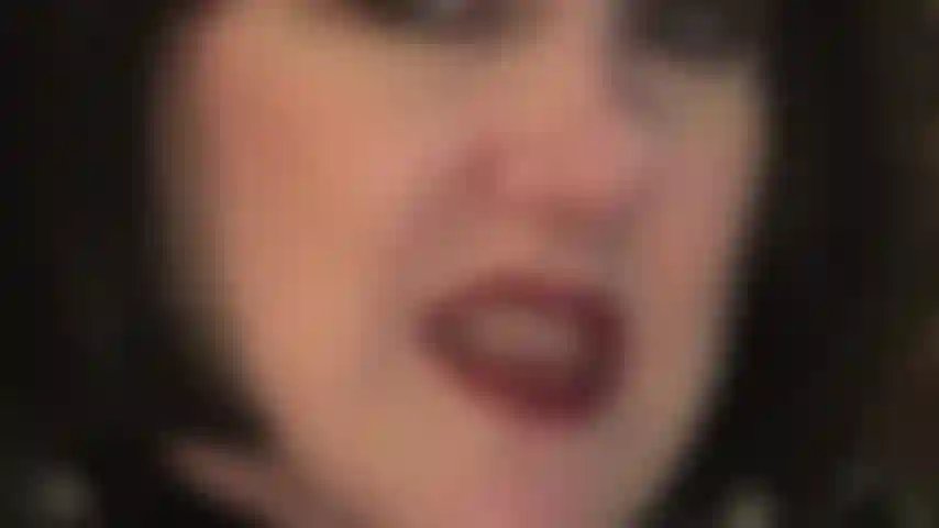 Con il viso in primo piano e una parrucca nera a caschetto, che mi stuzzica con il rossetto rosso sulle labbra, la lingua bagnata, i denti e le mani guantate di pelle che si divertirebbero a stringere i tuoi testicoli.