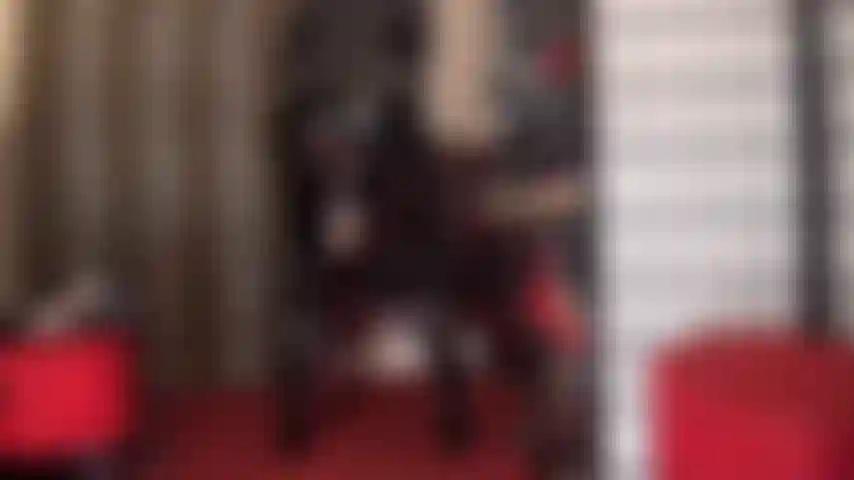 Una dea in pvc con una tuta nera lucida che mi stuzzica con il suo enorme pene bianco con strap-on che spunta da sotto la gonna.