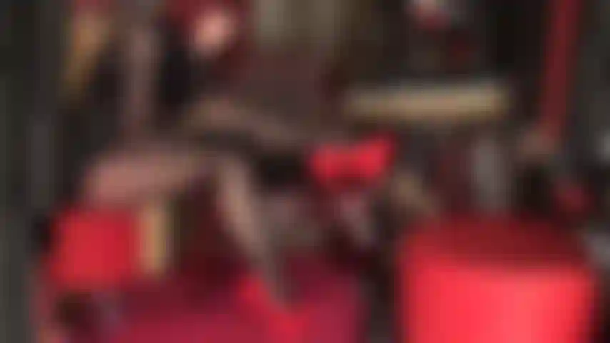 Con le gambe scollate in collant neri lucidi a strati, pelle e décolleté rosse con tacco a spillo. Con le gambe incrociate, rossetto nero, tacchi rossi.