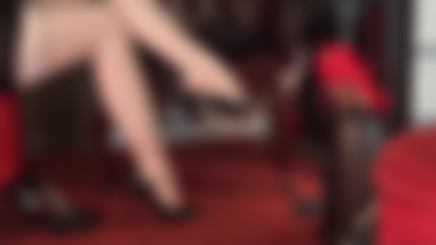 Collant color carne con giarrettiere e cuciture, gambe incrociate e piedi seducenti da cui pendono diverse paia di classiche décolleté.
