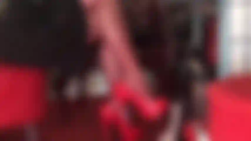 Seducenti gambe incrociate in collant rossi e scarpe rosse lucide stuzzicano il dolorante cazzo dello schiavo.