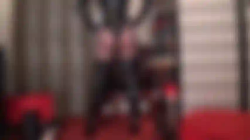 Curve splendenti di perfezione: una seduttrice splendente mostra le sue curve perfette in una tuta in pvc con perizoma, stivali alti sopra il ginocchio e collant neri trasparenti.