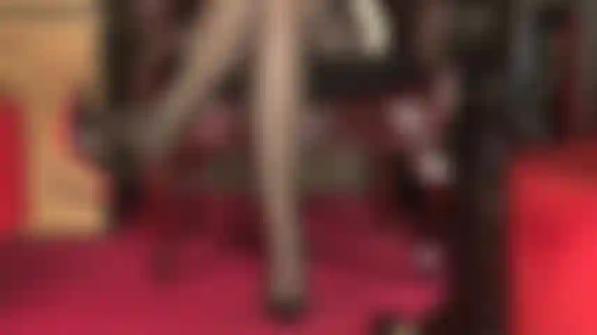 Una vista sexy su gambe coperte da calze, giarrettiere multi-cinturino che spuntano, cosce incrociate sexy e dita dei piedi che lasciano penzolare una décolleté con suola rossa.